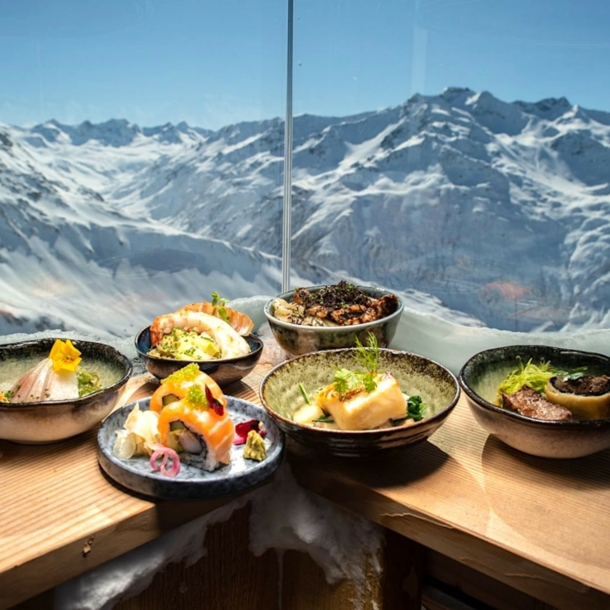 Japanisch angerichtete Teller auf einem Holztresen, im Hintergrund das Panorama von Andermatt