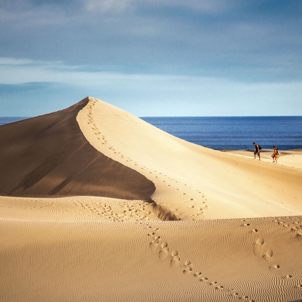 Zwei Personen wandern auf einer großen Sanddüne am Meer