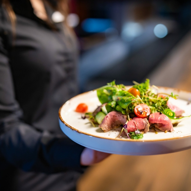 Eine Person hält einhändig einen Teller, auf dem ein Salat angerichtet ist.