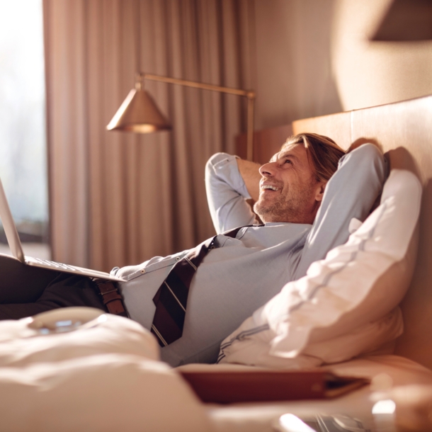 Ein Geschäftsmann liegt entspannt mit einem Laptop in einem Hotelbett