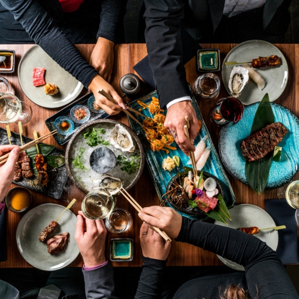 Hände nehmen mit Stäbchen Essen von Tellern in der Mitte eines Tisches