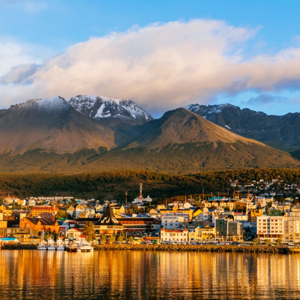 Stadtpanorama von Ushuaia am Wasser vor Bergkulisse im Sonnenuntergang