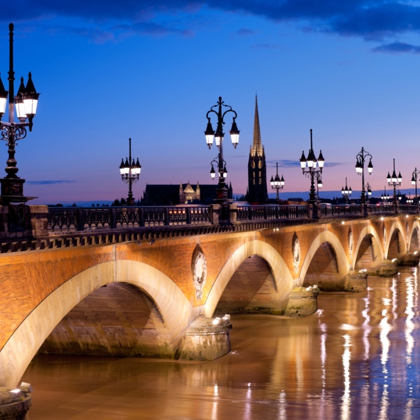 Eine alte Steinbrücke mit erleuchteten Straßenlaternen verläuft über einen Fluss in Bordeaux bei Nacht