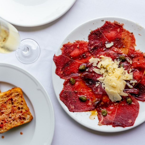 Weiße Teller mit geröstetem Brot und Carpaccio und ein Sektglas