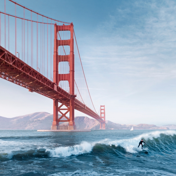 Ein Surfer auf einer Welle unter der roten Golden Gate Bridge