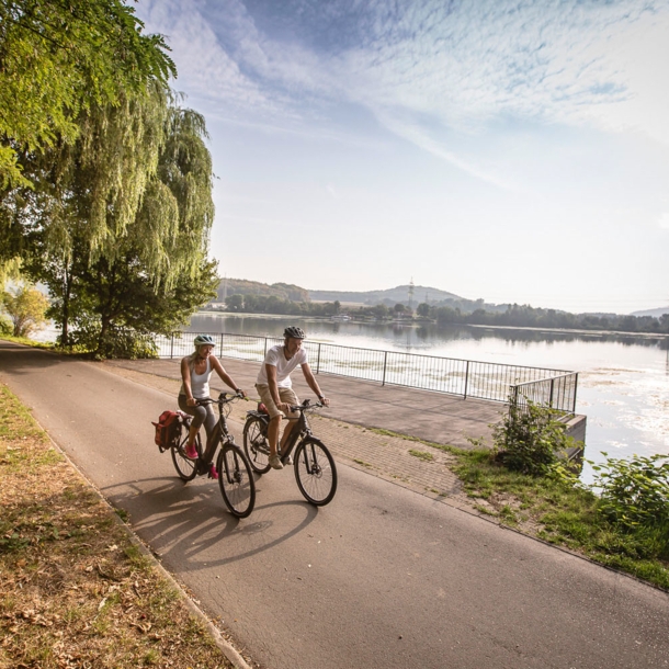 Ein Paar in Sommerkleidung fährt auf Fahrrädern auf einem Radweg entlang eines Flusses