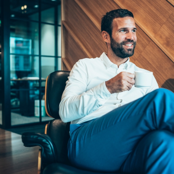 Ein Geschäftsmann sitzt entspannt mit einer Kaffeetasse in einem Sessel in einer Flughafen-Lounge