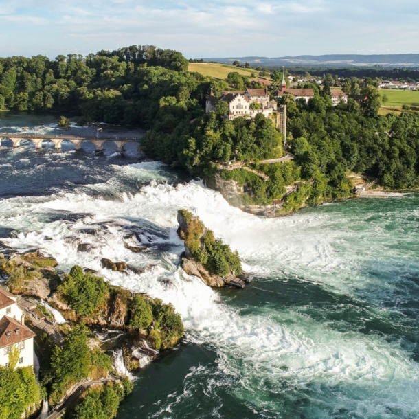 Luftaufnahme des Rheinfalls mit Schloss Laufen inmitten bewaldeter Natur