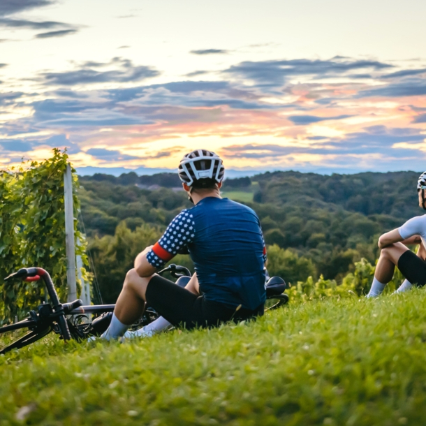 Rückenansicht zweier Personen in Fahrradkleidung, die auf einem Weinberg sitzen