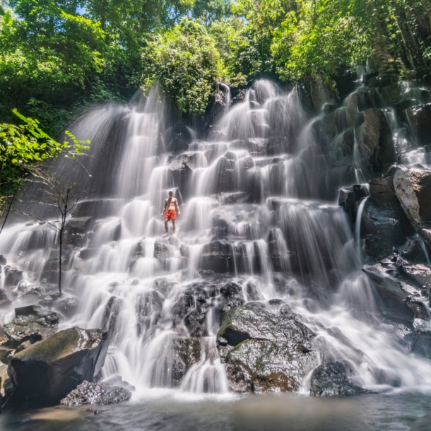 Eine Person in roter Badehose steht in einem gestuften Wasserfall