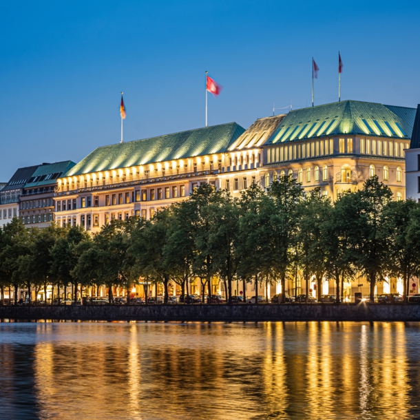 Beleuchtete Außenfassade des Hotels Vier Jahreszeiten am Wasser in der Dunkelheit.