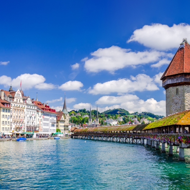 Altstadtpanorama von Luzern am Wasser mit einer hölzernen Brücke vor einem Wasserturm.