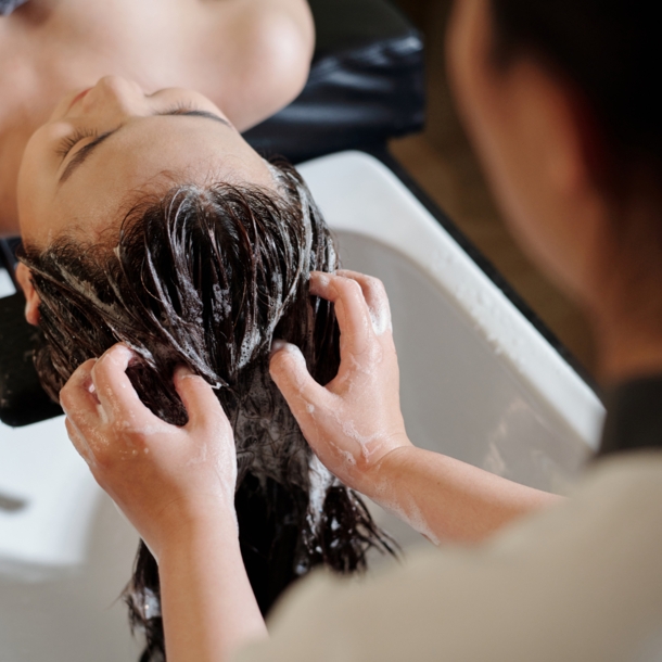 Die Haare einer liegenden Frau werden an einem Waschbecken von einer anderen Person gewaschen.