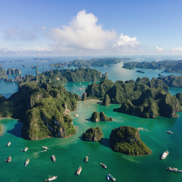 Aufnahme aus der Vogelperspektive von Booten und vielen kleinen von dichter Fauna bewachsenen Inseln in der vietnamesischen Halong-Bucht.