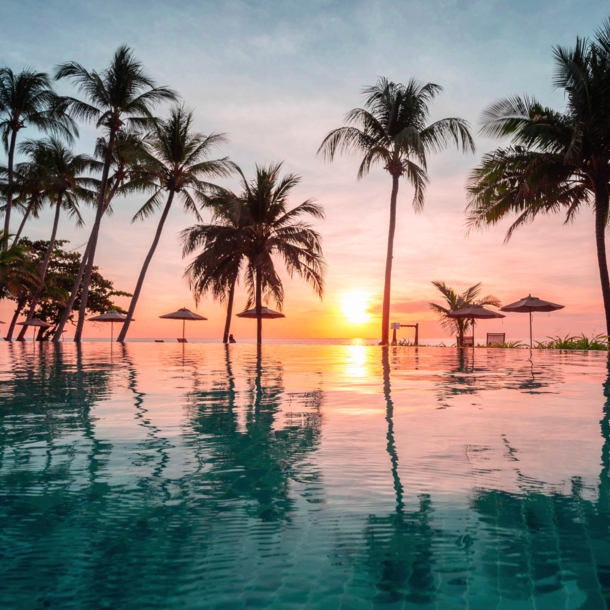 Palmengesäumter Infinity-Pool in einer Hotelanlage am Meer bei Sonnenuntergang.