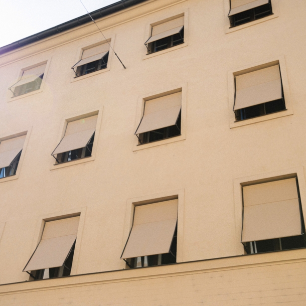 Hellbeige Hausfassade mit gleichfarbigen Markisen vor den Fenstern.