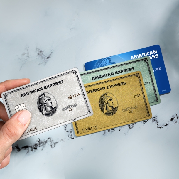 Eine Hand hält eine Platinum Card über eine goldene, grüne und blaue Kreditkarte von American Express.