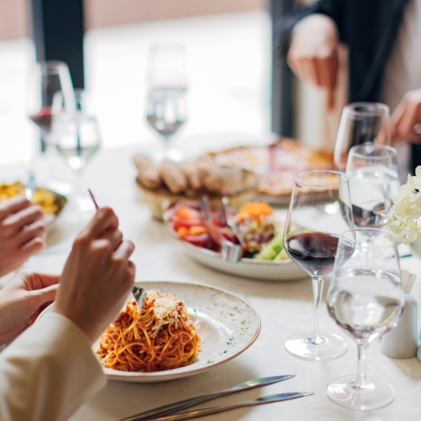 Eine Gruppe Personen an einem weiß eingedeckten Tisch in einem Restaurant mit verschiedenen Gerichten wie beispielsweise Pasta.