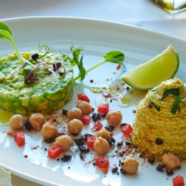 Ein weißer Porzellanteller mit einem Gericht aus Avocado, Kichererbsen, Limette und mehr im Restaurant brenner.