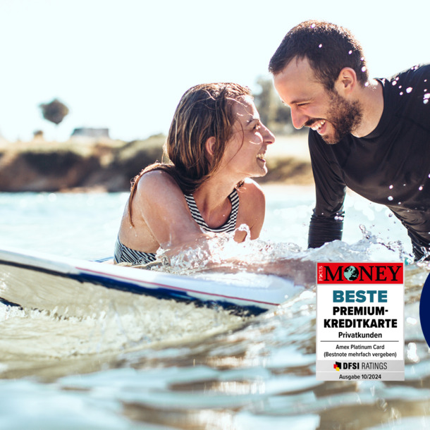 Ein lachendes Paar mit Surfboard im Meer.