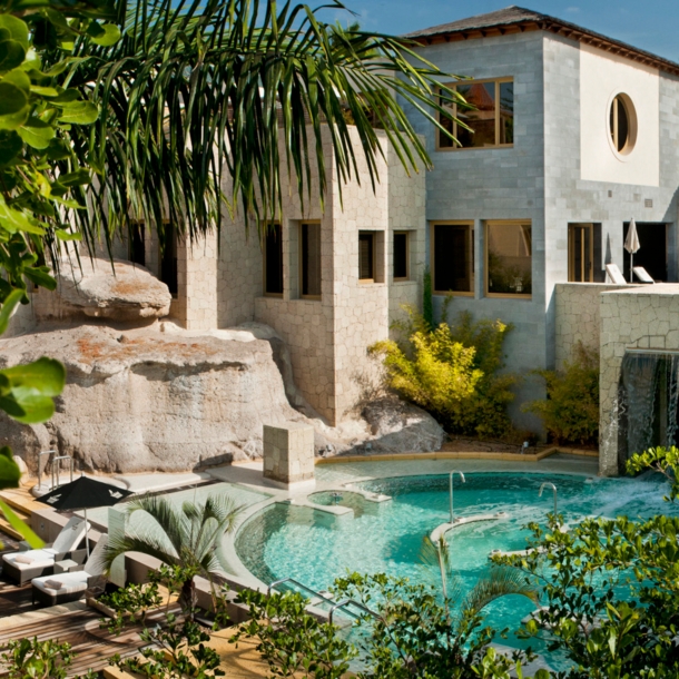 Resort des Bahia del Duque auf Teneriffa mit Poolanlage, Begrünung, Holzterrasse und Liegen.