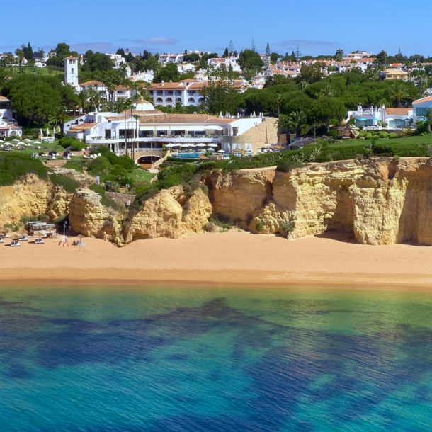 Luftaufnahme der Hotelanlage des Vila Vita Parc, das direkt an einer Klippe liegt. Darunter befindet sich ein Sandstrand und türkisblaues Meer.