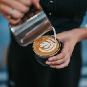 Milchschaum wird in einen Becher Kaffee geschüttet