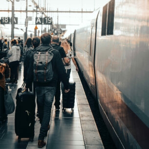 Reisende mit Gepäck laufen am Gleis in einem großen Bahnhof