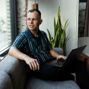 Benjamin Diedering sitzt mit Laptop auf dem Sofa und schaut aus dem Fenster