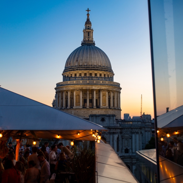 Belebtes Restaurant auf Dachterrasse vor der Kuppel der St Paul’s Kathedrale bei Abenddämmerung.