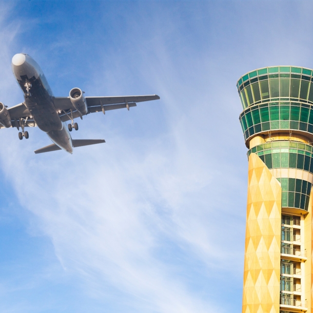 Untersicht eines Flugzeuges am blauen Himmel neben einem grün-gelben Tower. 