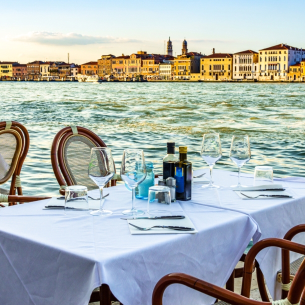 Ein gedeckter Tisch im Außenbereich eines Restaurants am Wasser in Venedig.