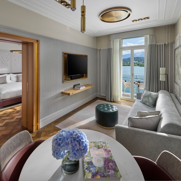 Elegante Hotelsuite mit Balkon an einem See vor Bergpanorama.