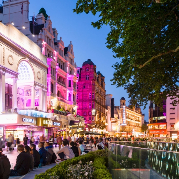 Belebter Leicester Square mit beleuchteter Häuserfassade am Abend.