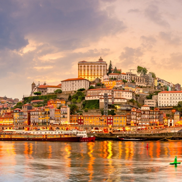 Panoramaaufnahme der Stadt Porto bei Sonnenuntergang mit dem Fluss Duoro im Vordergrund.