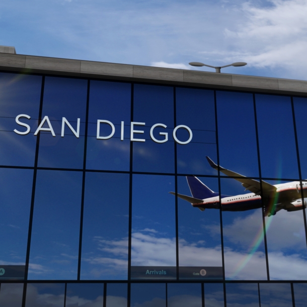 Flugzeug beim Abflug, das sich in den verspiegelten Fenstern einer Flughafenhalle spiegelt, auf denen die Aufschrift „San Diego“ zu lesen ist.