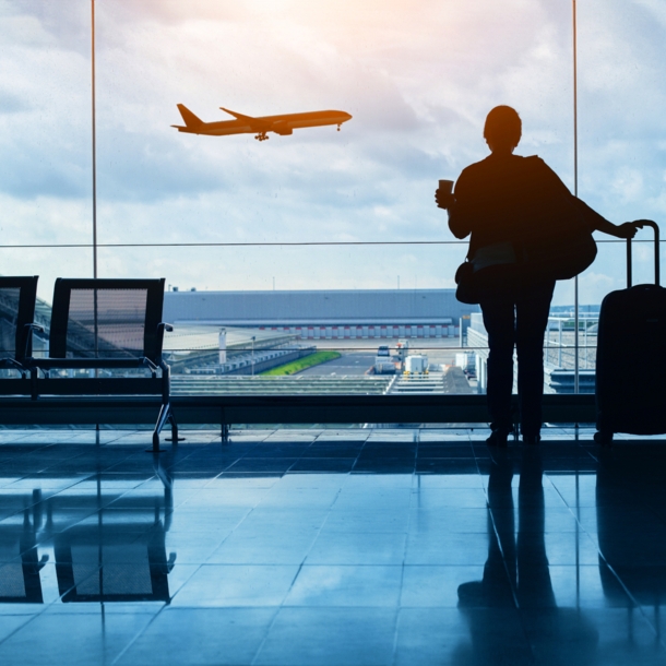 Silhouette einer Frau am Flughafen, die den Start eines Flugzeugs beobachtet.