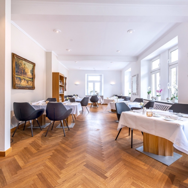 Heller Speisesaal eines gehobenen Restaurants mit Parkett und weiß eingedeckten Tischen.