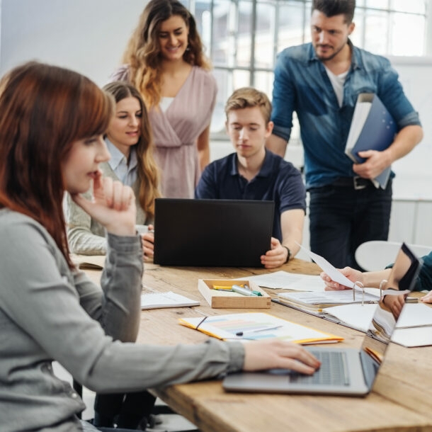 Mehrere Personen im hellen loftartigen Coworking-Space, stylishes Interieur, manche Personen konzentriert am Schreibtisch sitzend oder mit Laptop in einer Lounge-Zone, manche im Gespräch.