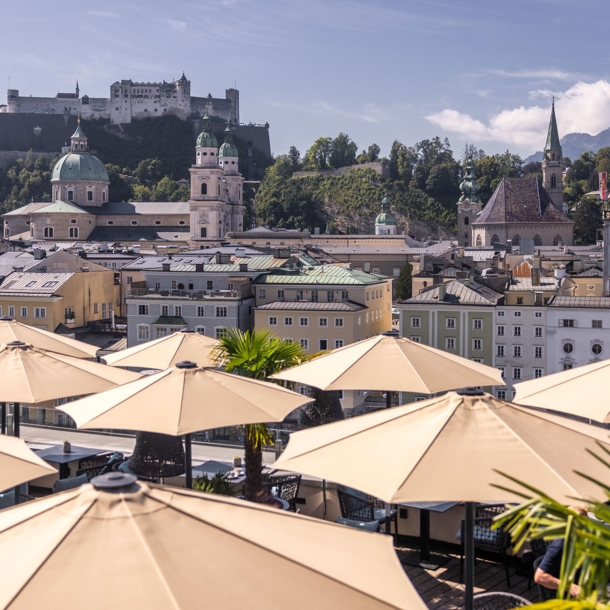 Panorama der Salzburger Altstadt mit Burg auf einem Berg am Fluss, im Hotelterrasse mit Sonnenschirmen.