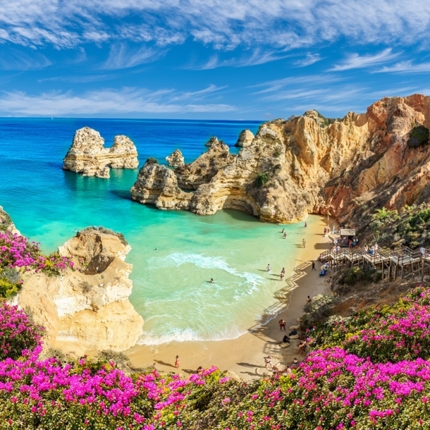 Blick von oben auf eine von Felsen umgebende Bucht und türkisblaues Meer an der Algarve.