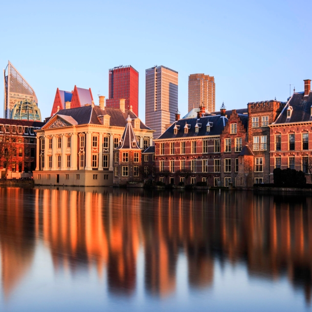 Skyline von Den Haag bei Sonnenuntergang, die Gebäude spiegeln sich im Wasser.