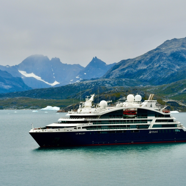 Das Bild zeigt im Vordergrund das Kreuzfahrtschiff. Im Hintergrund sind Berge und etwas Schnee und Eis zu sehen.