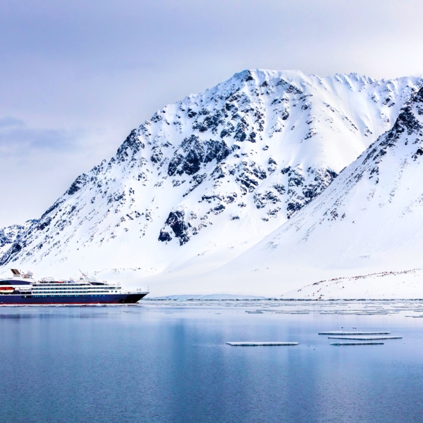 Ein Expeditionsschiff im arktischen Gewässer vor schneebedeckten Bergen.