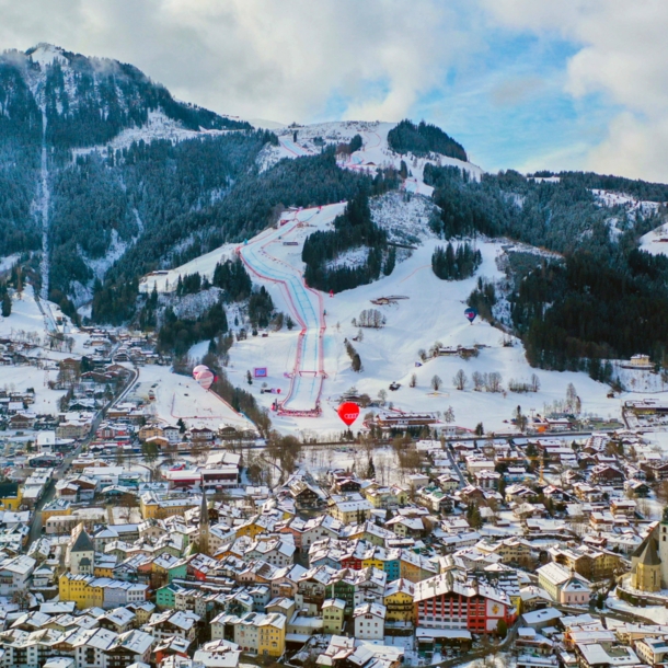 Schneebedecktes Stadtpanorama von Kitzbühel vor Berg mit Skipisten.