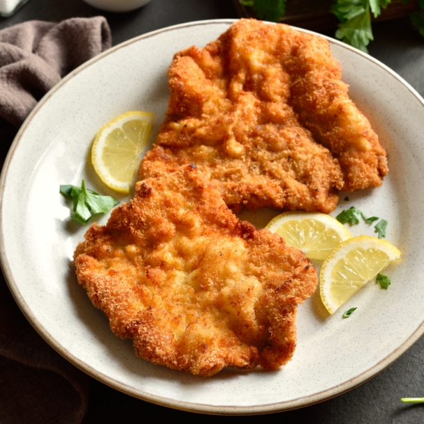 Ein Wiener Schnitzel auf einem Teller mit Zitronenscheiben.