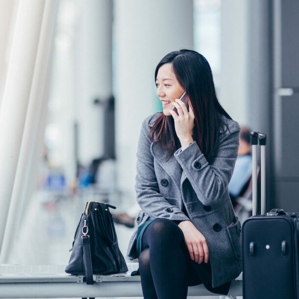 Eine asiatische Geschäftsfrau sitzt im Wartebereich eines Flughafens und telefoniert.