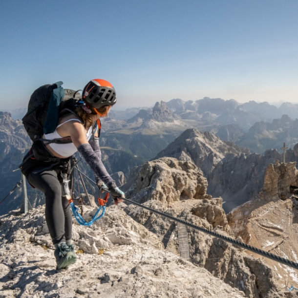 Eine Person mit Kletterausrüstung, die sich an einem Seil festhält, im Hintergrund Berge.