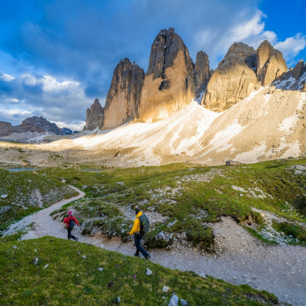 Zwei Personen beim Wandern, im Hintergrund Berge, blauer Himmel und Wolken.