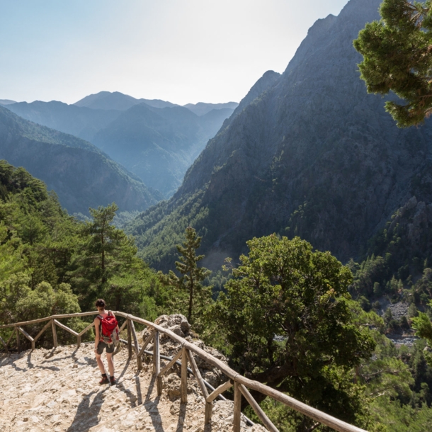 Eine Person beim Wandern in der Samaria-Schlucht auf Kreta, im Hintergrund Vegetation und Berggipfel.